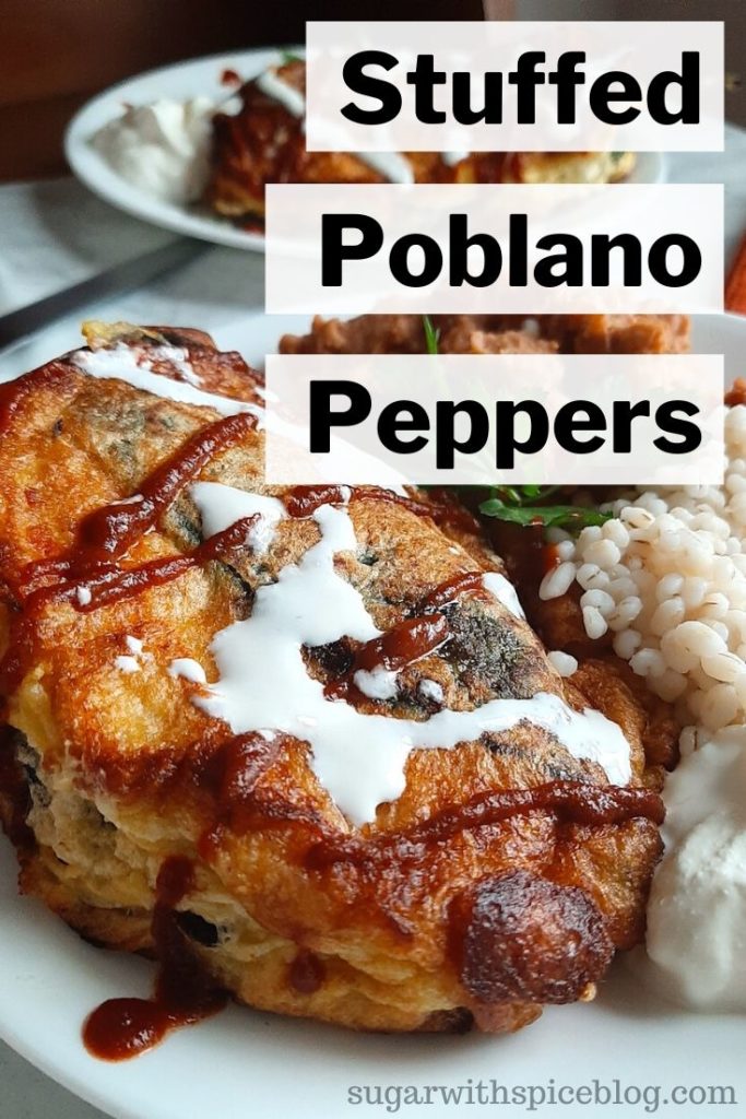 Shrimp and butternut squash stuffed poblano peppers on a white plate with refried beans and barley, drizzled with siracha and sour cream and cilantro. Sugar with Spice Blog.