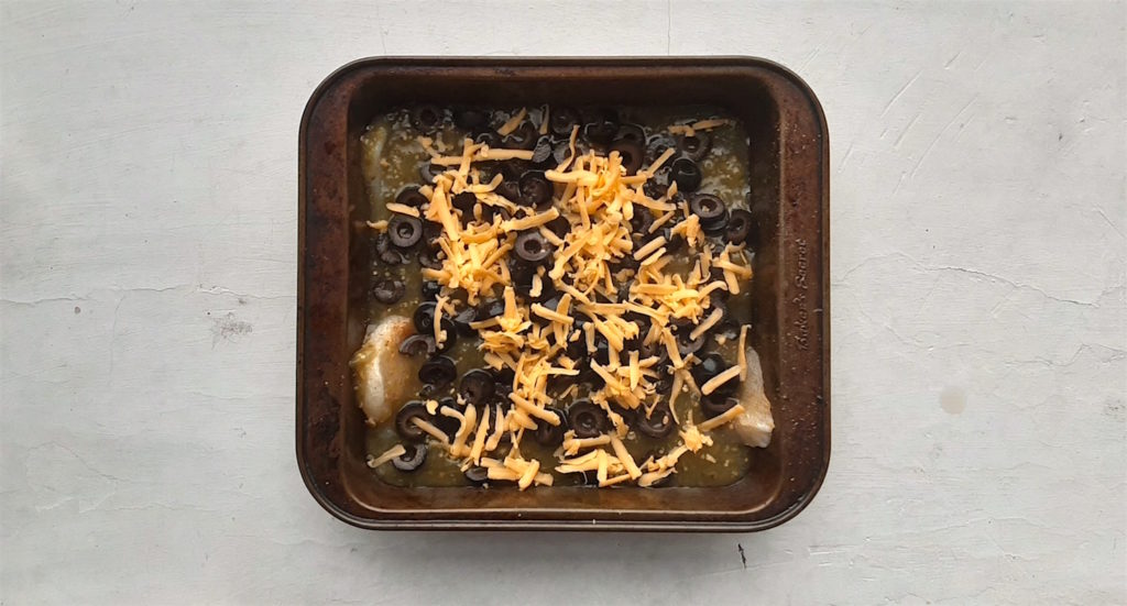 Basa filets topped with tomatillo sauce, black olives, and cheddar cheese in a casserole dish ready to go in the oven.