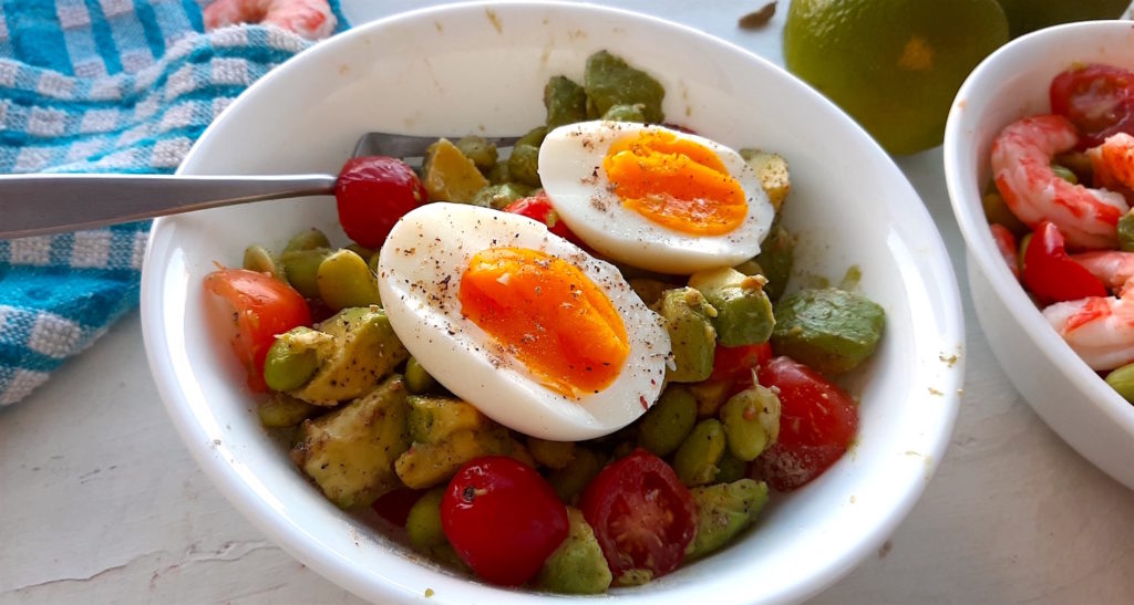 Protein salad with fresh edamame, sliced cherry tomatoes, sliced avocado, and a hard-boiled egg in a white bowl on a white background with blue checked cloth. Sugar with Spice Blog.