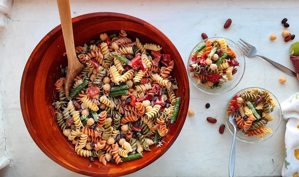 Three Bean Pasta Salad with lemony mustard dressing Sugar with Spice Blog. Overhead shot of Three Bean Pasta Salad in a big wooden salad bowl and wooden spoon with two small pyrex ramekins also holding salad on the right with two silver forks and some dish towels on a white surface.