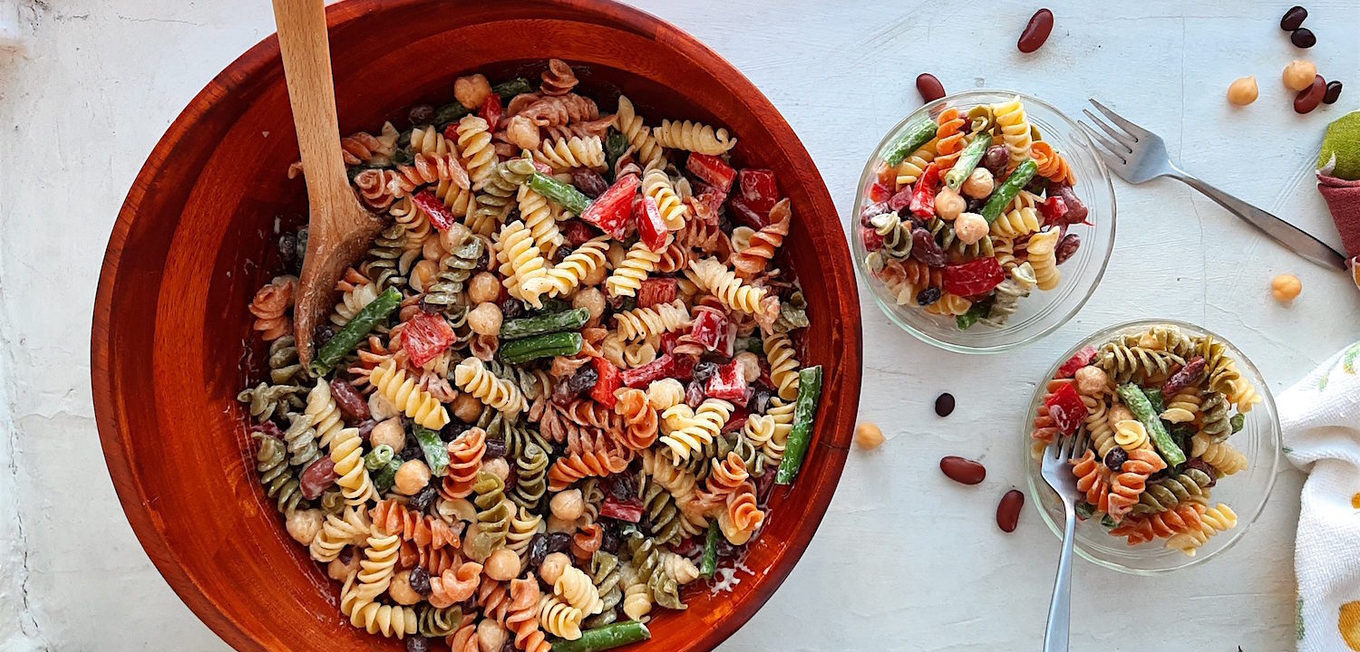 Three Bean Pasta Salad with lemony mustard dressing Sugar with Spice Blog. Overhead shot of Three Bean Pasta Salad in a big wooden salad bowl and wooden spoon with two small pyrex ramekins also holding salad on the right with two silver forks and some dish towels on a white surface.