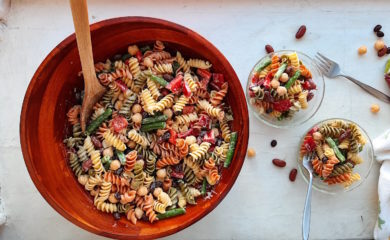 Three Bean Pasta Salad with lemony mustard dressing Sugar with Spice Blog. Overhead shot of Three Bean Pasta Salad in a big wooden salad bowl and wooden spoon with two small pyrex ramekins also holding salad on the right with two silver forks and some dish towels on a white surface.