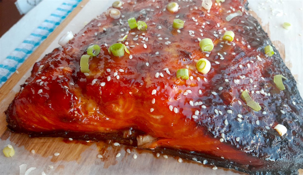 Honey and Wasabi Glazed Salmon close up topped with sesame seeds and sliced green scallions on a wooden cutting board with blue checked dish towel in the background. Sugar with Spice Blog.