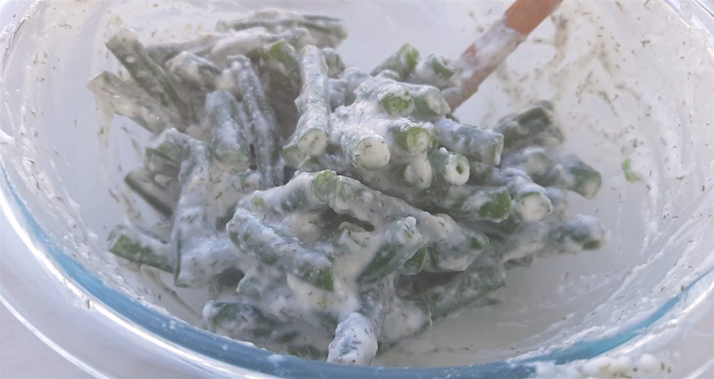 Green beans in yogurt and dill in a pyrex bowl and mixing spatula on a white background. Sugar with Spice Blog.