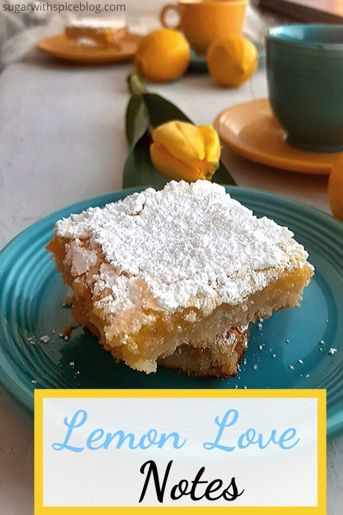 Lemon Love Note pinterest image. Two Lemon bars on a blue saucer with yellow tulip, lemon, and mismatched blue and yellow tea cup and saucer on a white window sill. Lace curtain and reversed cups and saucers behind. Sugar with Spice Blog