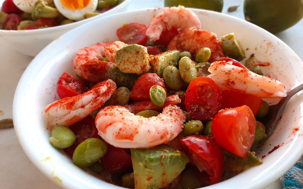 Fresh protein salad with edamame beans, fresh tomatoes, fresh avocado, lightly steamed shrimp and paprika and lime in a white bowl. Sugar with Spice Blog.