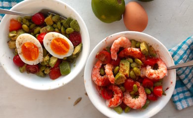 Protein Salad with edamame, sliced cherry tomatoes, avocado, eggs, and shrimp in two white bowls with silver forks on a white window sill with blue checked towels.