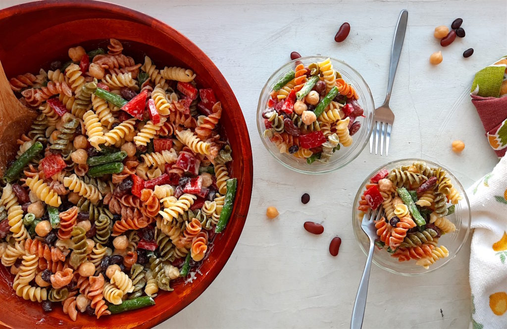 Three Bean Pasta Salad with lemony mustard dressing Sugar with Spice Blog. Overhead shot of Three Bean Pasta Salad in a big wooden salad bowl and wooden spoon with two small pyrex ramekins also holding salad on the right with two silver forks and some dish towels on a white surface.