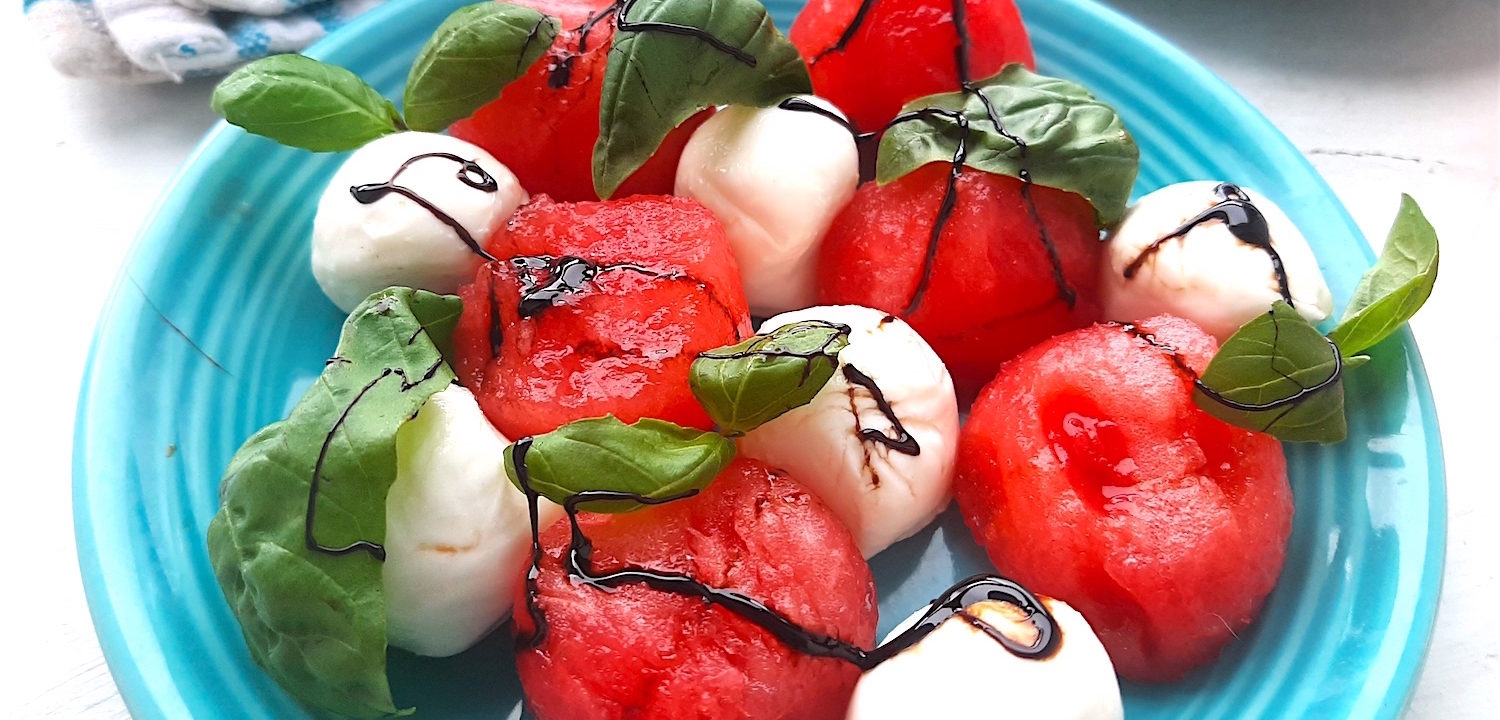 Summer Watermelon Salad close up of watermelon balls, mozzarella balls, basil leaves, balsamic reduction on a blue plate. Sugar with Spice Blog.