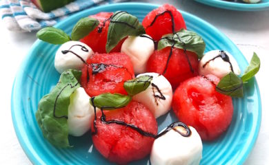 Summer Watermelon Salad close up of watermelon balls, mozzarella balls, basil leaves, balsamic reduction on a blue plate. Sugar with Spice Blog.