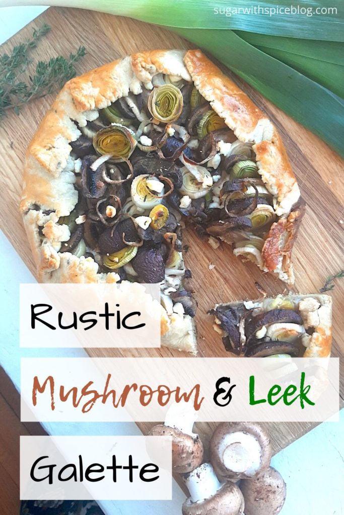 Overhead shot of Mushroom Leek Galette with goat cheese and thyme wrapped in all butter crust on a wooden cutting board. Surrounded by leeks, thyme and mushrooms. One slice cut out to the side. Pinterest Image. Sugar with Spice Blog.
