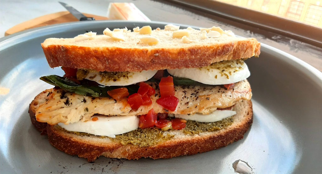 Chicken Caprese Panini before cooking. Peasant bread, pesto, crushed tomatoes, fresh basil and mozzarella, seasoned chicken breast in a nonstick sauté pan waiting to cook. Sugar with Spice Blog.