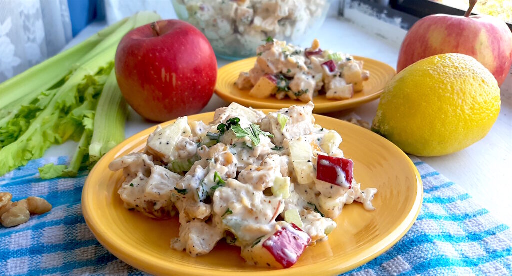 Chicken Salad with Apples and Walnuts served on yellow plates on a blue checked cloth with apples, celery and lemons in the background. Wide front shot. Shot. Sugar with Spice Blog.