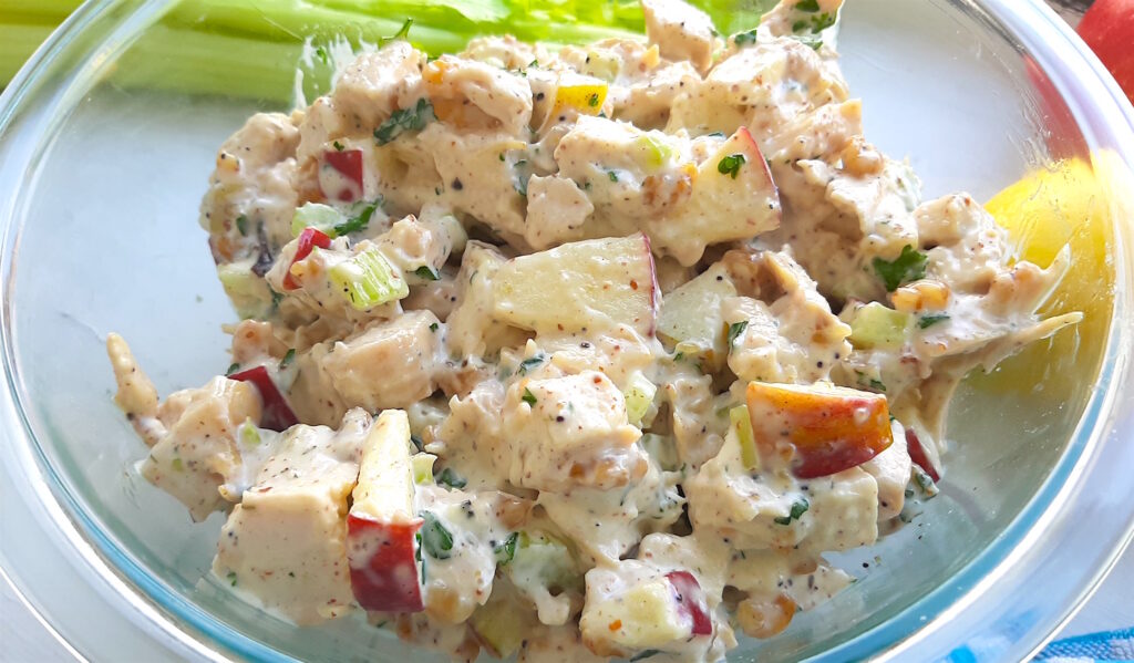 Chicken Salad with Apples and Walnuts in a clear pyrex dish with apples, celery and lemons in the background. Close Up Shot. Sugar with Spice Blog.