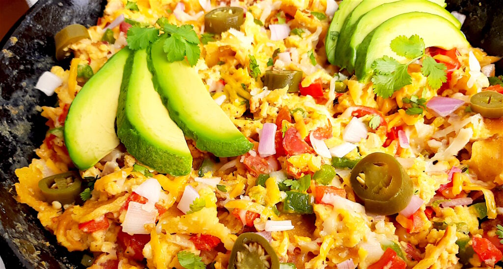 Classic Tex-Mex Migas topped with avocado, pickled jalapeños, and sliced avocado in a cast iron skillet. Close Up shot. Sugar with Spice Blog.