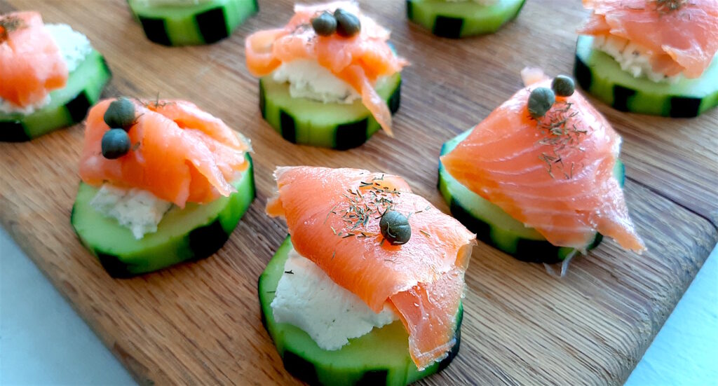 Cucumber Smoked Salmon Bites on a wooden cutting board with boursin cheese, capers, and smoked salmon. Wide shot. Sugar with Spice Blog.