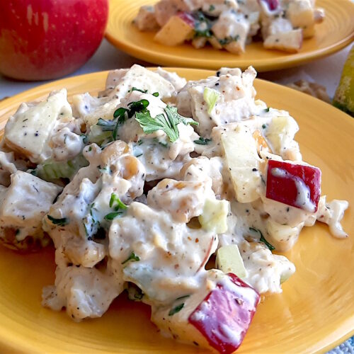 Chicken Salad with Apples and Walnuts served on yellow plates on a blue checked cloth with apples, celery and lemons in the background. Close Up Shot. Sugar with Spice Blog.