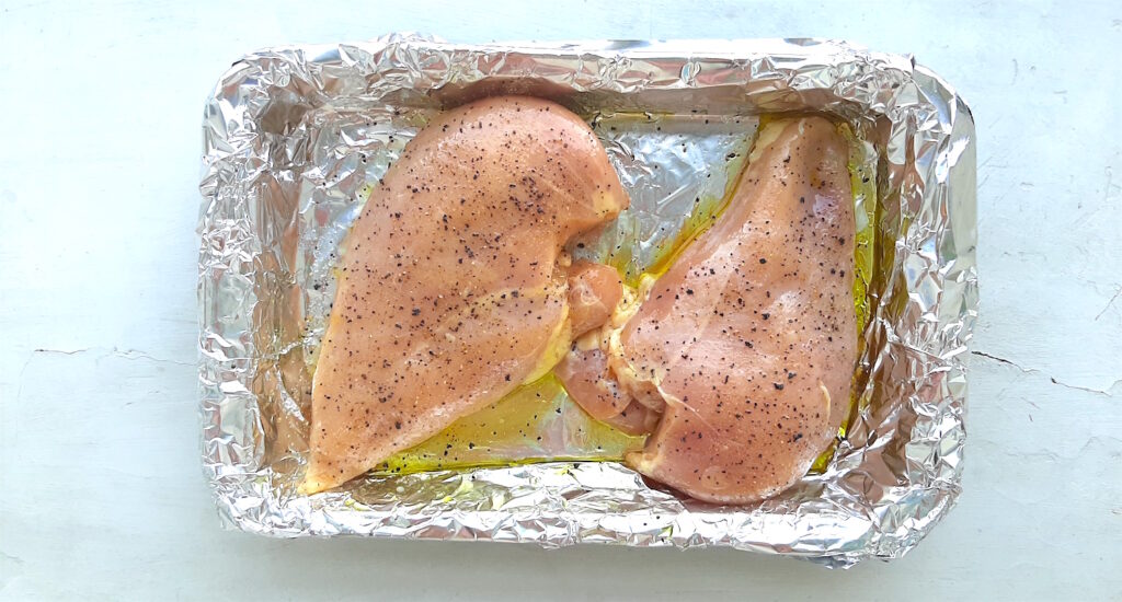 Chicken breast read to cook for chicken salad, placed in a casserole dish with tinfoil olive oil and spices. Sugar with Spice Blog.