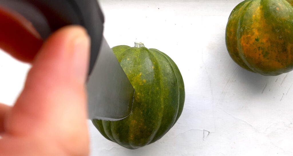 Cutting an acorn squash, length-wise. Knife placed in the center of the squash by a woman's hand. White background. Sugar with Spice Blog.