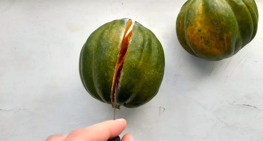 Cutting an acorn squash, length-wise. Knife pulled down to the top of the squash by a woman's hand. White background. Sugar with Spice Blog.