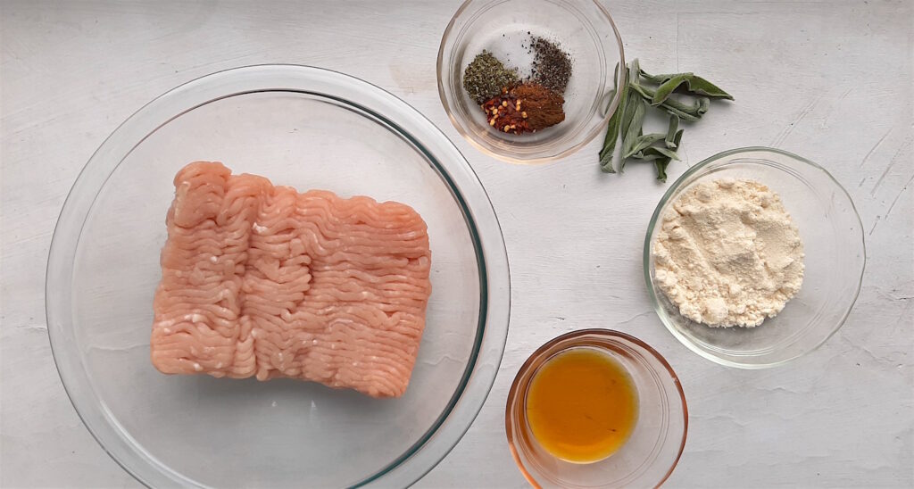 Homemade turkey sausage ingredients on a white background: ground turkey, maple syrup, fresh sage, seasoning, almond flour. Sugar with Spice Blog.