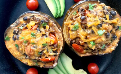 Mexican-style stuffed acorn squash with beans, corn, tomatoes, beef, and cheddar cheese. Two served together in a cast iron skillet with fresh sliced avocado and cherry tomatoes surrounding. Overhead shot. Sugar with Spice Blog.