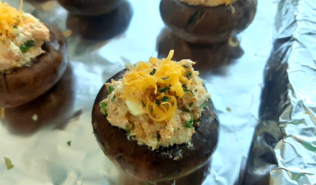 Crab stuffed mushrooms, raw, waiting to go in the oven. Topped with grated cheddar, bread crumbs, and dried parsley on a tin-foil covered baking sheet. Sugar with Spice Blog.