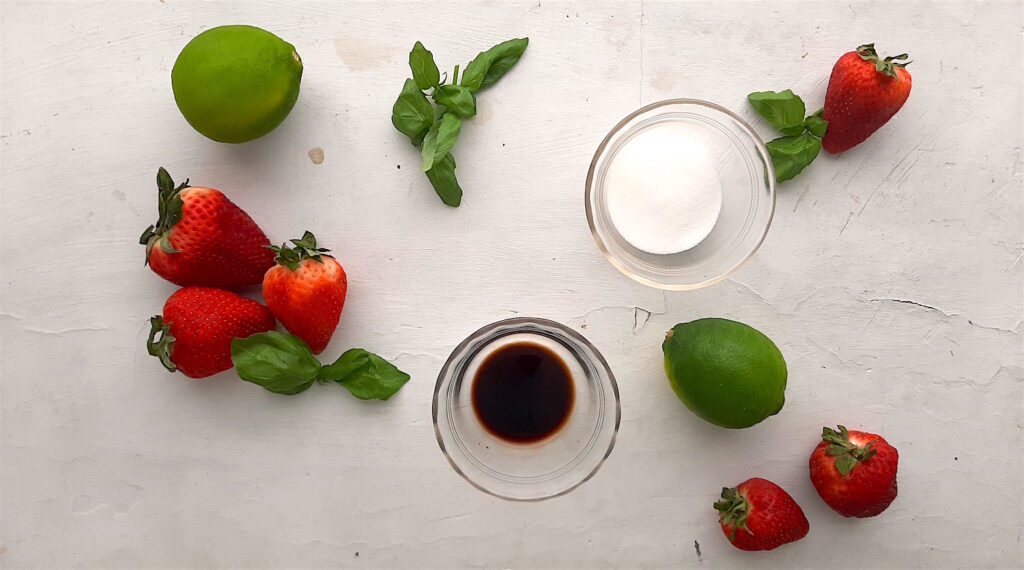 Balsamic Strawberry Basil Mojito ingredients on a white window sill, fresh strawberries, basil, limes, balsamic vinegar, and sugar. Overhead wide shot. Sugar with Spice Blog.