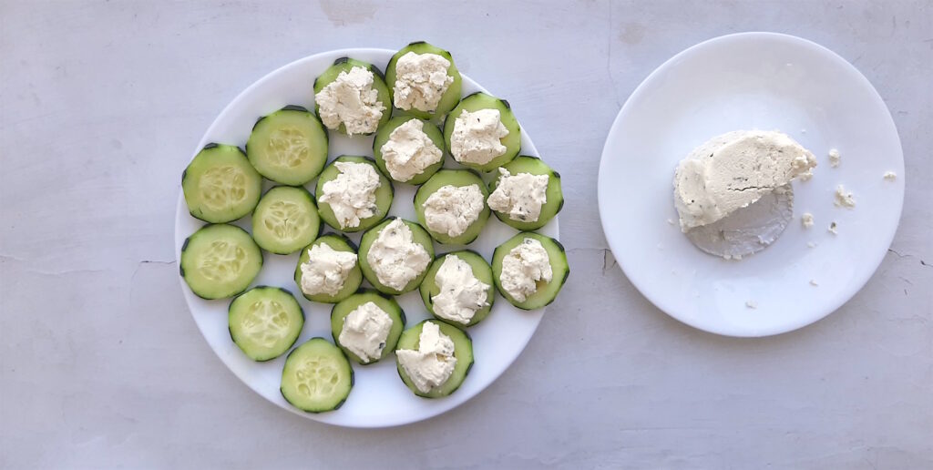 Cucumber Smoked Salmon Bites being prepared by scooping boursin cheese on each sliced cucumber. On a white background. Sugar with Spice Blog.