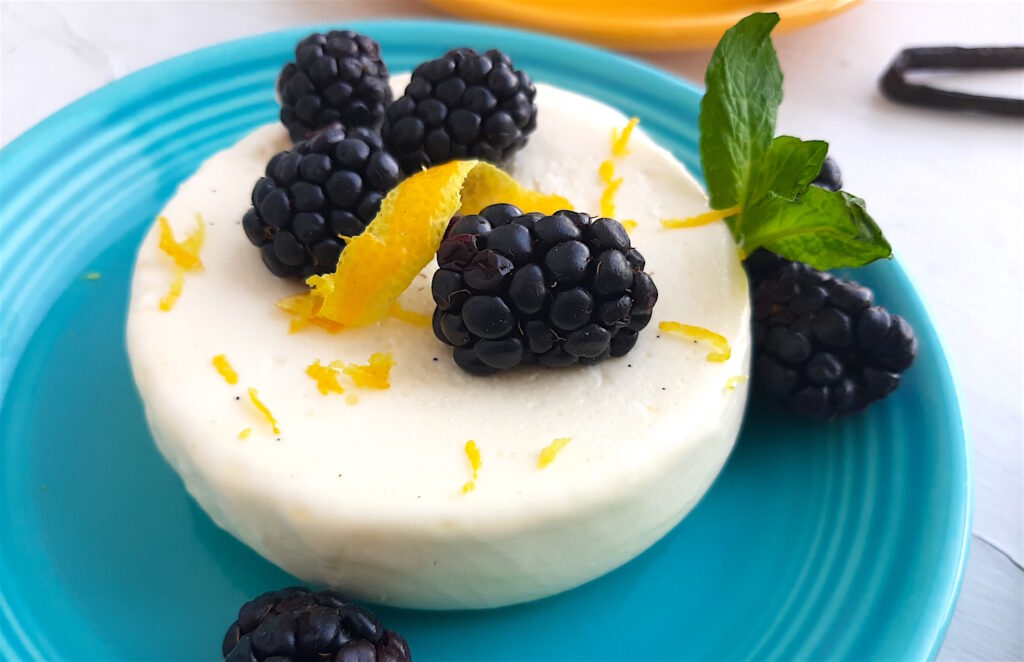 Vanilla Bean Panna Cotta on a blue plate with fresh lemon zest and spiraled lemon skin, fresh blackberries and mint. Sugar with Spice blog.