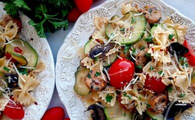 Smoked Sausage and Veggie Bow Tie Pasta Skillet with bow tie pasta, smoked sausage slices, mushrooms, zucchini slices, and halved cherry tomatoes on two white plates. Fresh parsley and cherry tomatoes to the side. White background, overhead shot. Sugar with Spice Blog.