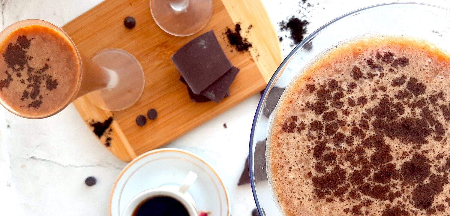 Mocha Martini Recipe Sugar with Spice Blog, One large mocha martini on a white background with espresso powder and chocolate chips in the background. Two smaller mocha martinis on a wooden cutting board with chocolate and an espresso in a white cup and saucer with dried flowers to the side.