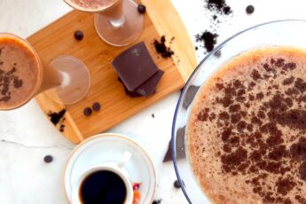 Mocha Martini Recipe Sugar with Spice Blog, One large mocha martini on a white background with espresso powder and chocolate chips in the background. Two smaller mocha martinis on a wooden cutting board with chocolate and an espresso in a white cup and saucer with dried flowers to the side.