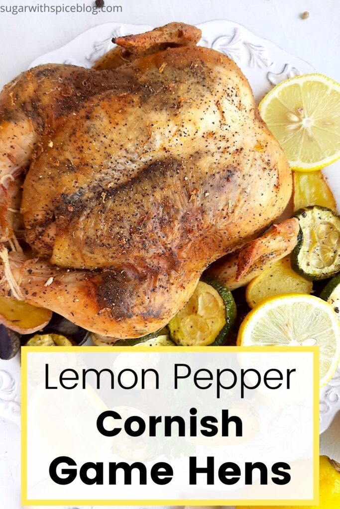 Lemon Pepper Cornish Hen on a white plate with assorted mixed veggies like potatoes, zucchini rounds, mushrooms, and onions on the side. Lemon rounds and parsley for garnish. Whole lemons, garlic cloves, and pepper kernels on the side, white background. Overhead shot. Pinterest Image. Sugar with Spice Blog.