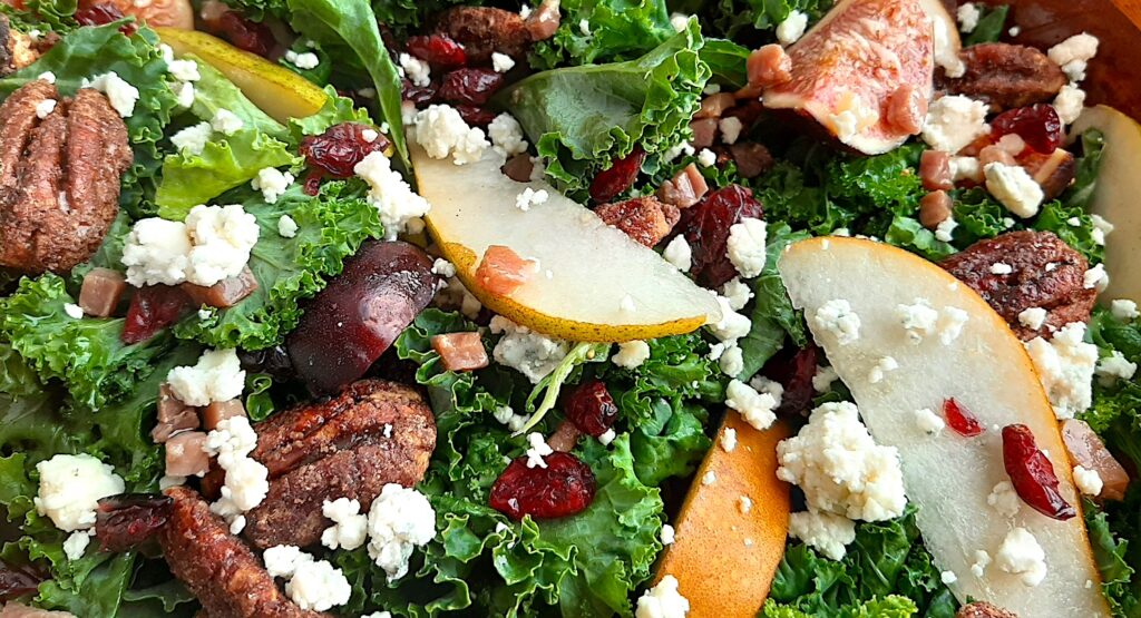 Winter Pear Salad in a brown wooden bowl, ingredients separated including: sliced d'anjou pears, sliced bosc pears, gorgonzola, dried cranberries, quartered figs, sautéed pancetta, maple candied pecans, and kale. All on a white background. Closeup shot. Sugar with Spice Blog.