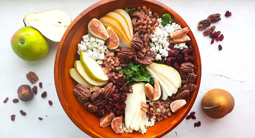 Winter Pear Salad in a brown wooden bowl, ingredients separated including: sliced d'anjou pears, sliced bosc pears, gorgonzola, dried cranberries, quartered figs, sautéed pancetta, maple candied pecans, and kale. Fresh d'anjou pears, bosc pear, mission fig, maple candied pecans, and dried cranberries surround. All on a white background. Overhead shot. Sugar with Spice Blog.