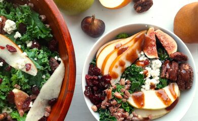 Winter Pear Salad in a white ceramic bowl bowl, ingredients separated including: sliced d'anjou pears, sliced bosc pears, gorgonzola, dried cranberries, quartered figs, sautéed pancetta, maple candied pecans, and kale. Drizzled with cranberry balsamic dressing. More winter pear salad, tossed, in a wooden bowl to the left, half in frame. Fresh d'anjou pears, bosc pear, mission fig, maple candied pecans, and dried cranberries surround. All on a white background. Overhead shot. Sugar with Spice Blog.