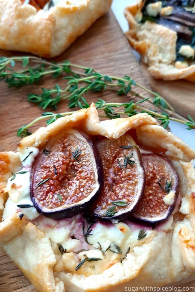 Mini Savory Galette of fig, goat cheese, thyme, and honey on a wooden cutting board with assorted mini savory galettes and fresh thyme behind. Overhead front shot. Sugar with Spice Blog. Pinterest Image.