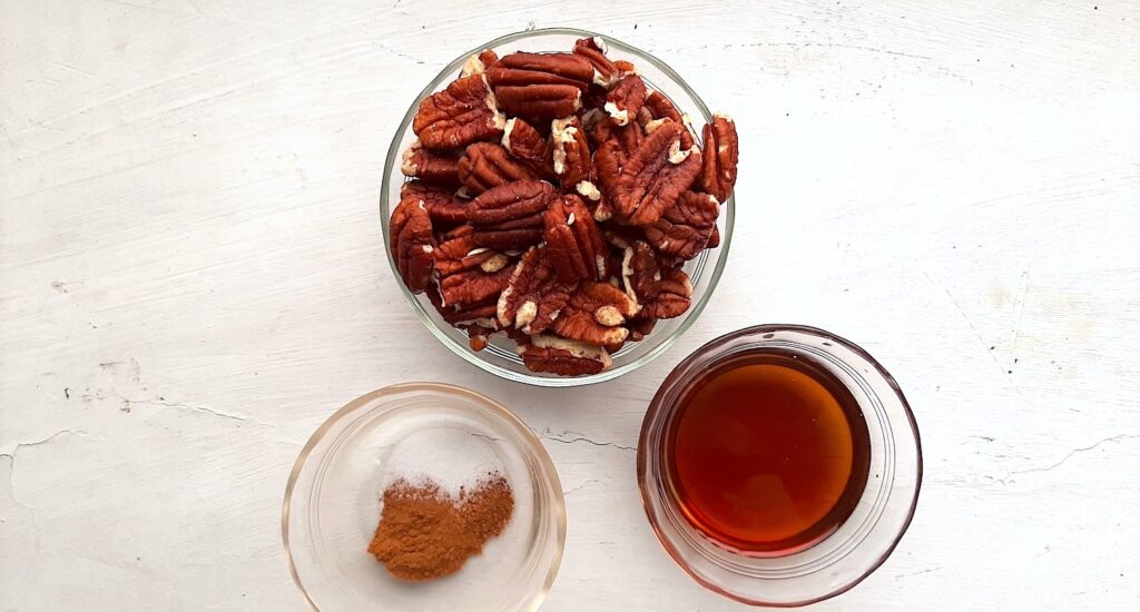 Maple candied pecan ingredients. Pecans in a pyrex dish. Salt, cinnamon, and nutmeg in a pyrex dish, maple syrup in a pyrex dish. Sugar with Spice Blog.