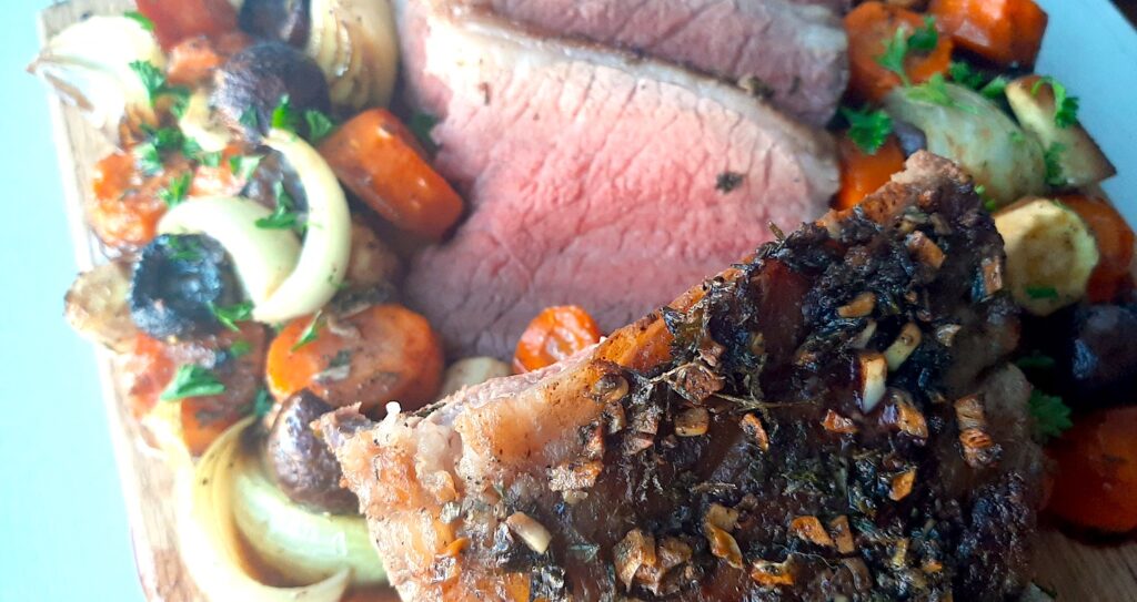 Garlic and Herb Bottom Round Roast Beef on a cutting board, several medium rare slices displayed. Surrounded by roasted carrots, parsnips, onions, and mushrooms. Sprinkled with fresh parsley. Sugar with Spice Blog.