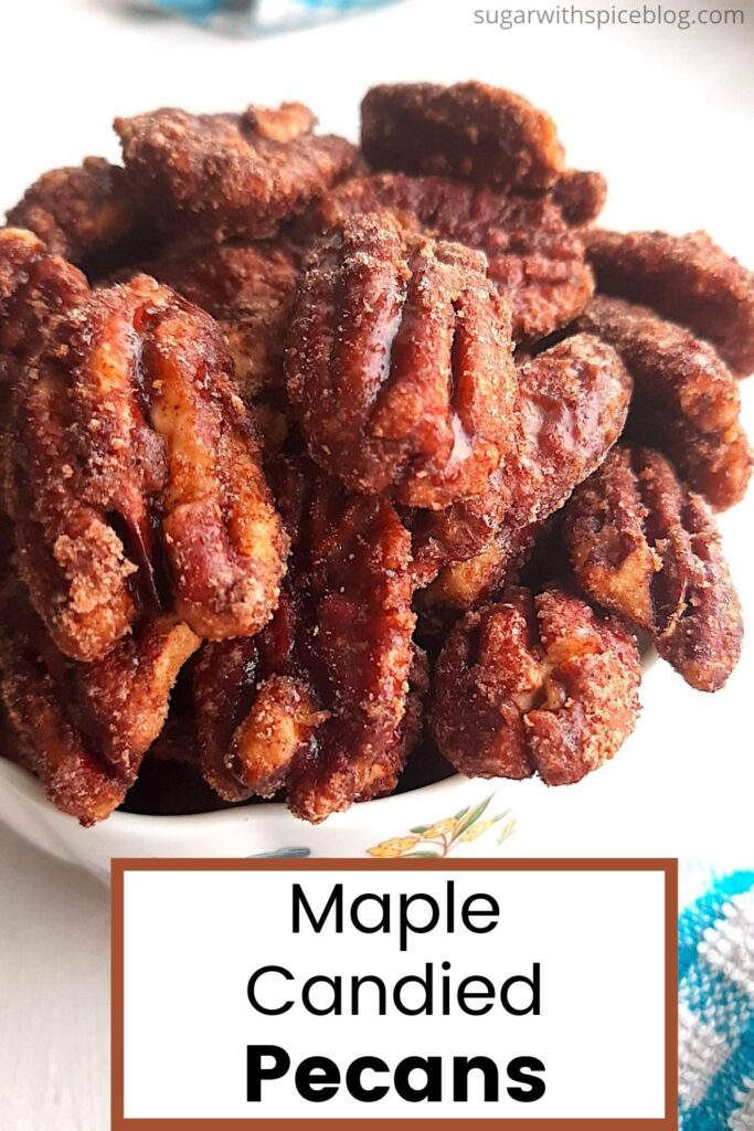 Maple candied pecans in a small cream bowl with a blue checked dish towel behind. All on the white background. Close up. Text overlay with brown border says maple candied pecans. Pinterest Image. Sugar with Spice Blog.