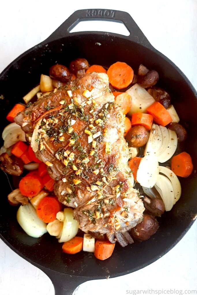 Bottom Round Roast Beef with garlic herb butter rub on a layer of carrots, parsnips, mushrooms, and onions in a large cast iron skillet. White background, overhead shot. Pinterest Image. Sugar with Spice Blog.